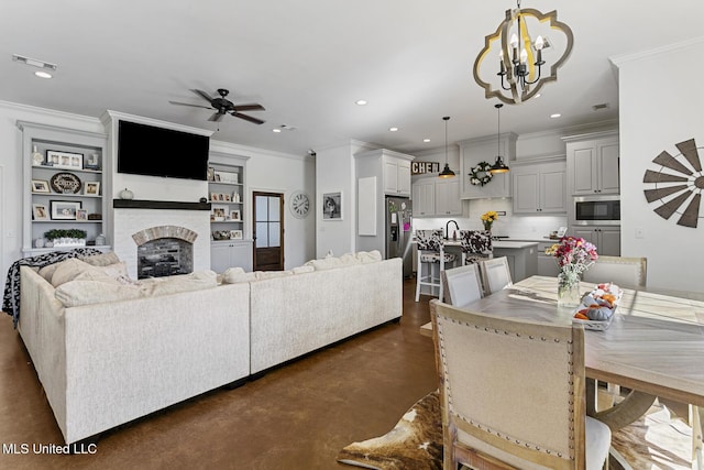 dining area with ornamental molding, a brick fireplace, sink, and ceiling fan with notable chandelier