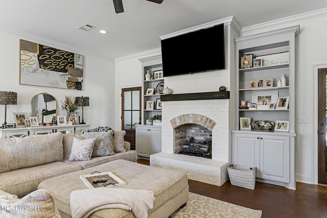 living room with built in shelves, crown molding, a brick fireplace, dark hardwood / wood-style flooring, and ceiling fan