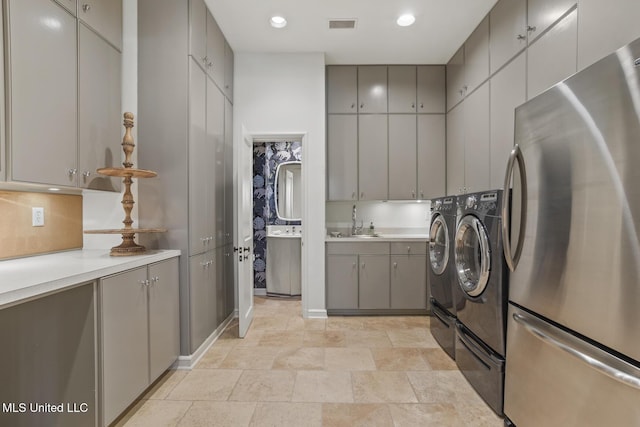 kitchen with stainless steel fridge, washer and clothes dryer, sink, and gray cabinetry