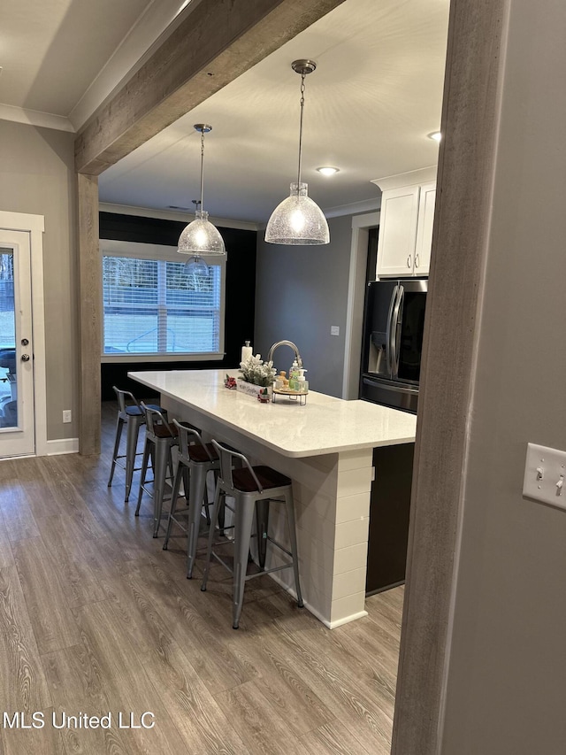 kitchen with a center island with sink, a breakfast bar area, pendant lighting, and white cabinets