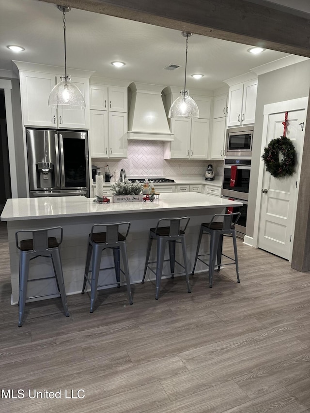 kitchen featuring pendant lighting, white cabinetry, appliances with stainless steel finishes, and custom range hood