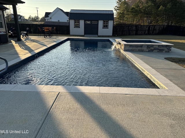 view of pool featuring an in ground hot tub, pool water feature, an outbuilding, and a patio area