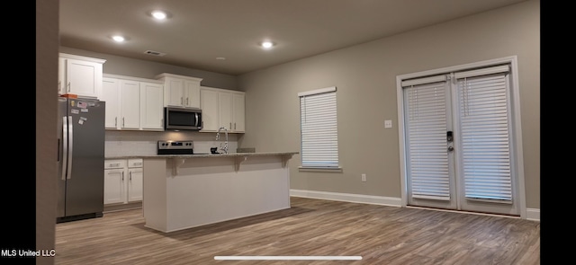 kitchen featuring a breakfast bar area, light stone countertops, an island with sink, white cabinetry, and stainless steel appliances