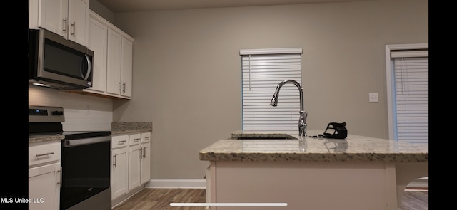 kitchen featuring dark wood-type flooring, light stone counters, a center island with sink, white cabinets, and appliances with stainless steel finishes