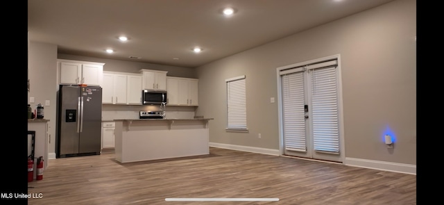 kitchen with a center island, white cabinets, light wood-type flooring, a kitchen bar, and stainless steel appliances