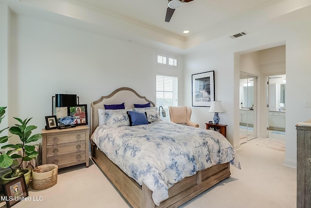 bedroom featuring light carpet, ensuite bath, visible vents, a ceiling fan, and a raised ceiling