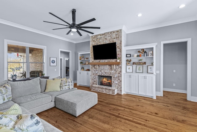 living room featuring baseboards, ceiling fan, ornamental molding, light wood-type flooring, and a brick fireplace