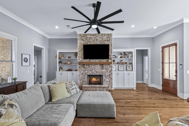 living room with baseboards, a ceiling fan, wood finished floors, crown molding, and a brick fireplace