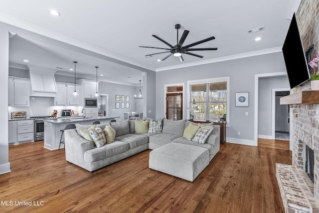 living area with dark wood-style flooring, crown molding, a fireplace, visible vents, and a ceiling fan