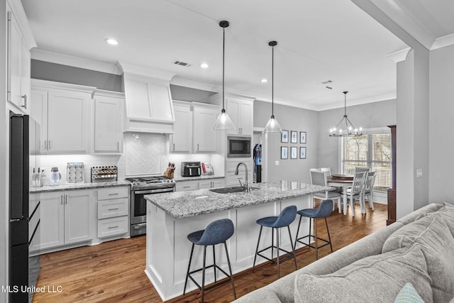 kitchen with stainless steel range with gas cooktop, built in microwave, a sink, black refrigerator, and premium range hood