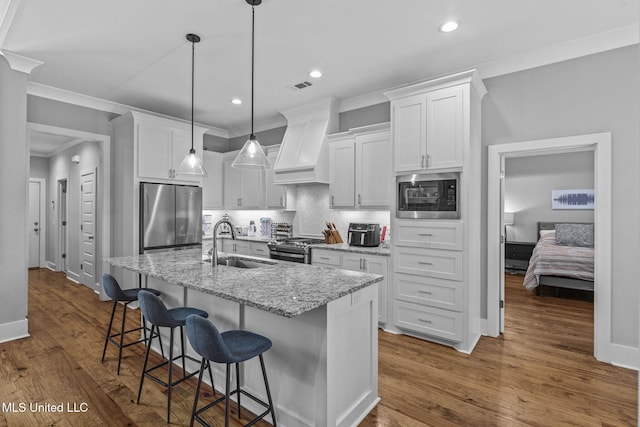 kitchen featuring white cabinets, stainless steel appliances, premium range hood, a kitchen bar, and a sink