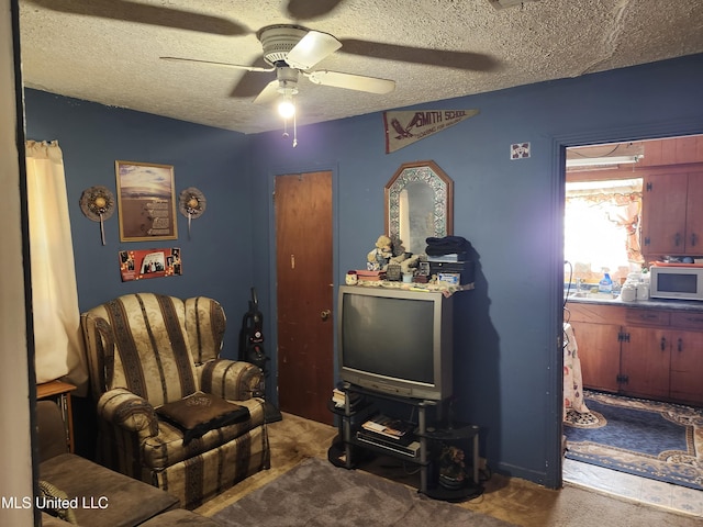 sitting room featuring ceiling fan, a textured ceiling, and dark colored carpet