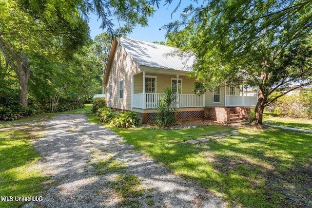 view of front facade with covered porch, metal roof, gravel driveway, and a front yard