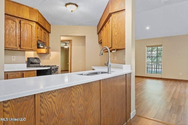 kitchen with gas range oven, brown cabinetry, a sink, light wood-type flooring, and under cabinet range hood