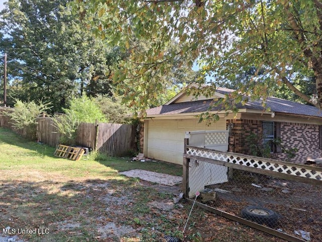 view of side of property featuring fence, a yard, a shingled roof, a garage, and brick siding