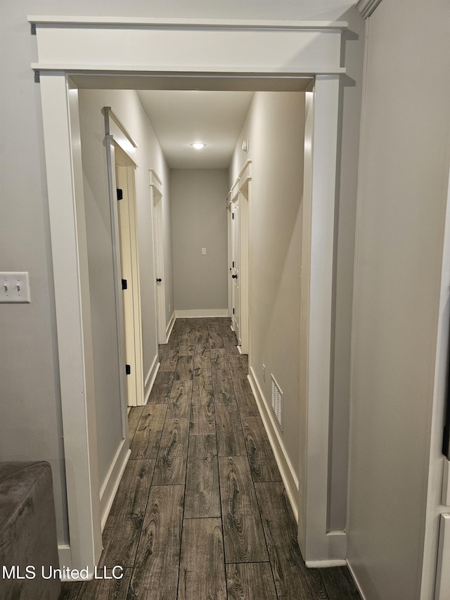 hallway featuring dark wood-type flooring, visible vents, and baseboards