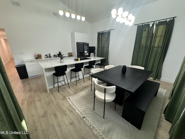 dining area with an inviting chandelier, high vaulted ceiling, and light wood-type flooring