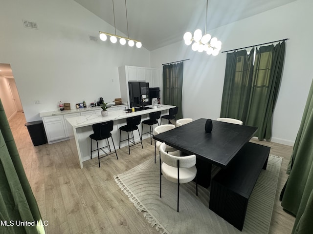 dining space with light wood-type flooring, an inviting chandelier, and high vaulted ceiling