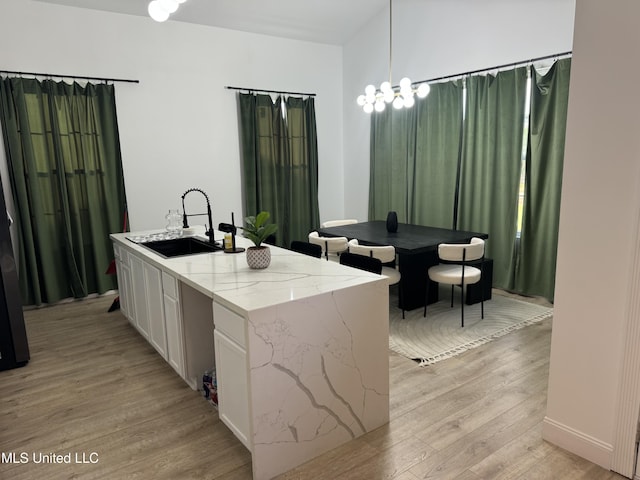 kitchen featuring light stone counters, sink, decorative light fixtures, light hardwood / wood-style floors, and white cabinetry