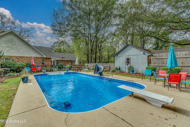 view of swimming pool featuring a diving board, a water slide, and a patio area