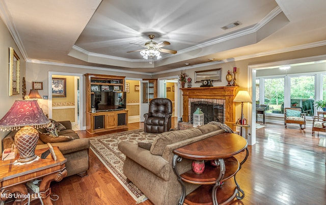 living room with hardwood / wood-style flooring, a raised ceiling, and ornamental molding