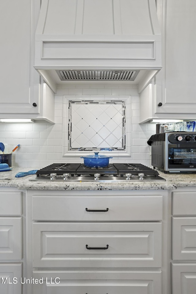 kitchen featuring white cabinetry, custom exhaust hood, light stone counters, and backsplash