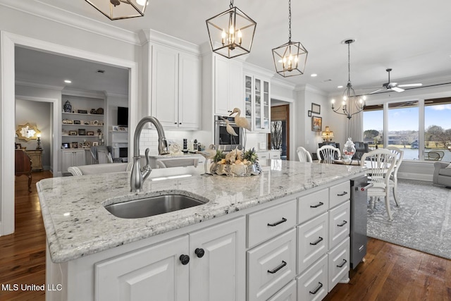 kitchen featuring a sink, white cabinetry, hanging light fixtures, a center island with sink, and crown molding