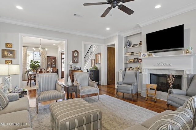 living room with built in features, a fireplace, visible vents, ornamental molding, and wood finished floors