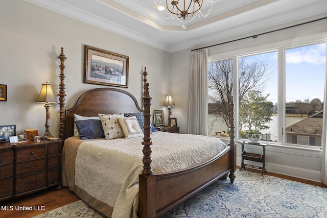 bedroom with baseboards, a raised ceiling, ornamental molding, wood finished floors, and a chandelier