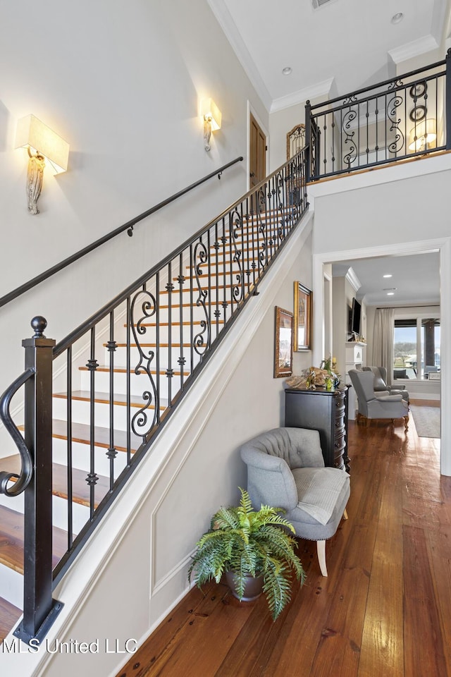 stairs with a high ceiling, crown molding, and wood finished floors