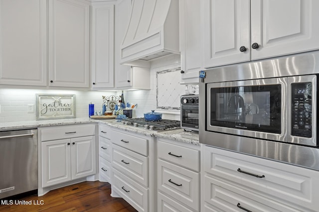 kitchen with stainless steel appliances, white cabinets, custom exhaust hood, light stone countertops, and dark wood finished floors