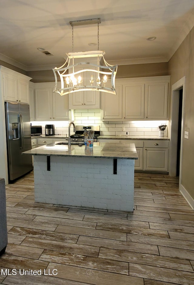 kitchen with an island with sink, white cabinetry, stainless steel appliances, and hanging light fixtures