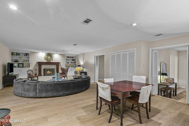 dining room with built in shelves, ornamental molding, light hardwood / wood-style floors, and a brick fireplace