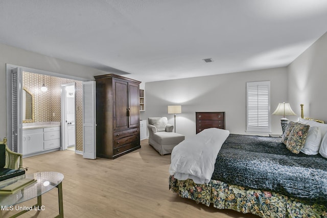 bedroom featuring connected bathroom and light hardwood / wood-style flooring