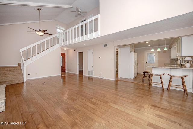 unfurnished living room featuring ceiling fan, light hardwood / wood-style floors, high vaulted ceiling, and sink