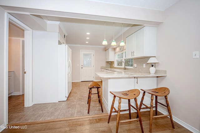 kitchen with a kitchen breakfast bar, white refrigerator with ice dispenser, kitchen peninsula, white cabinets, and backsplash