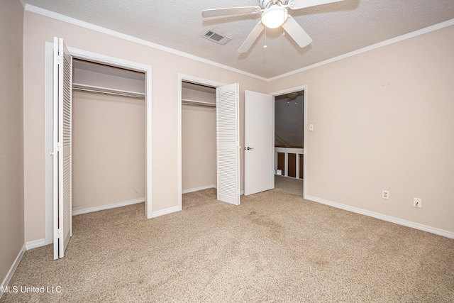 unfurnished bedroom with a textured ceiling, multiple closets, ceiling fan, ornamental molding, and light colored carpet