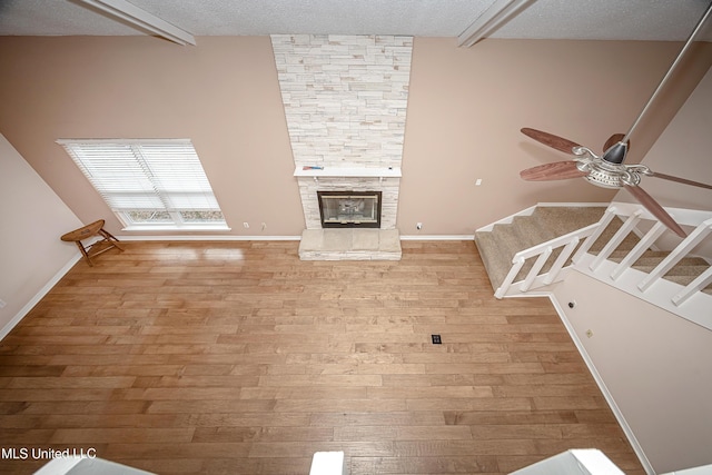 unfurnished living room featuring ceiling fan, light wood-type flooring, beamed ceiling, and a fireplace