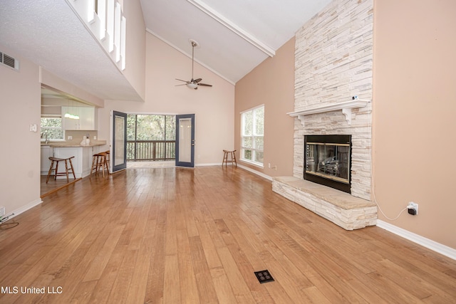 unfurnished living room featuring a fireplace, beamed ceiling, ceiling fan, light hardwood / wood-style flooring, and high vaulted ceiling