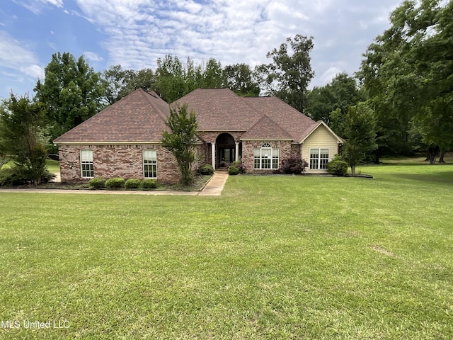 french country home with a front yard, a shingled roof, and brick siding