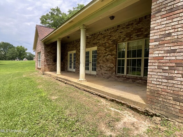 view of home's exterior with french doors, brick siding, a lawn, and a patio