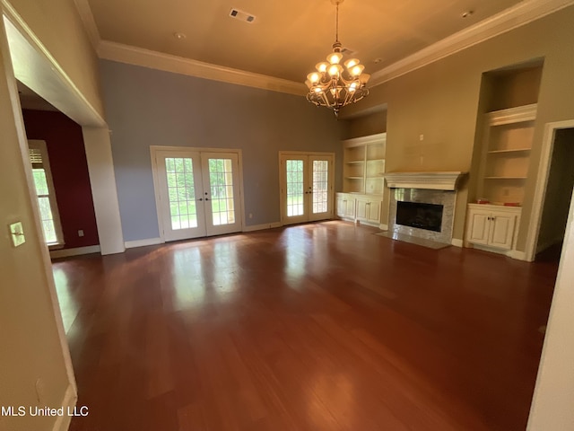 unfurnished living room with french doors, a chandelier, ornamental molding, built in shelves, and wood finished floors