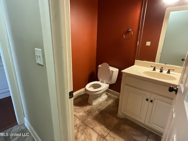 half bathroom with tile patterned flooring, toilet, vanity, and baseboards