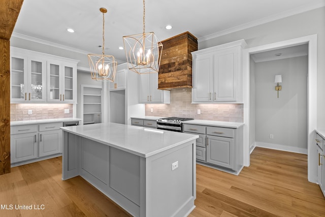 kitchen featuring glass insert cabinets, light countertops, hanging light fixtures, a center island, and stainless steel range with gas stovetop