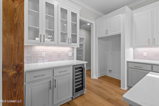 kitchen with beverage cooler, light countertops, glass insert cabinets, and crown molding