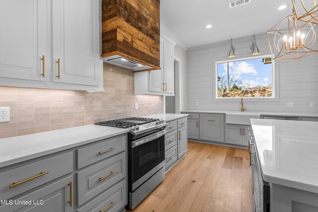 kitchen featuring light wood finished floors, light countertops, hanging light fixtures, gas stove, and a sink