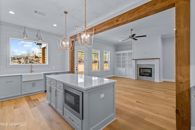 kitchen with a kitchen island, open floor plan, built in microwave, pendant lighting, and a sink