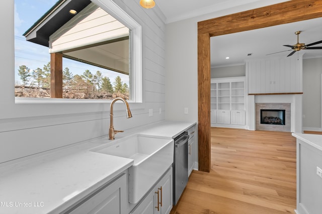 kitchen with light countertops, stainless steel dishwasher, a fireplace, and a sink