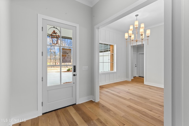 doorway featuring light wood-style floors, a chandelier, crown molding, and baseboards