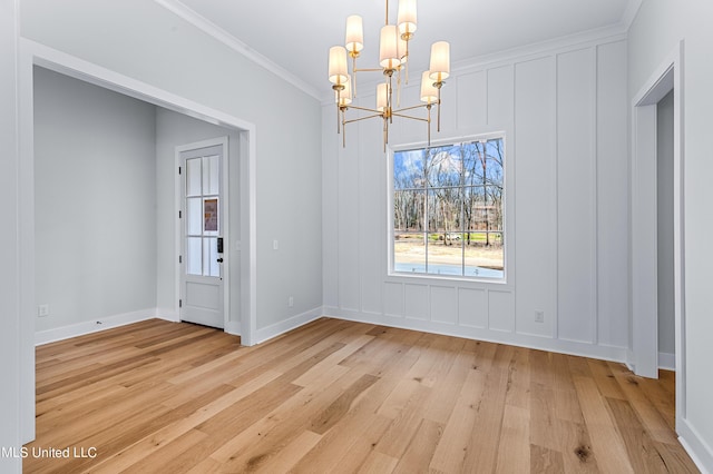 unfurnished dining area featuring light wood-style flooring, a decorative wall, a notable chandelier, baseboards, and ornamental molding